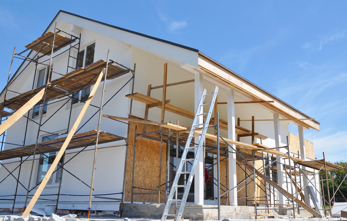 House renovation with wall insulation, plastering, paiting walls. House construction with scaffolding outdoor.